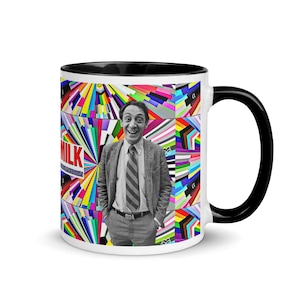 May include: A white ceramic mug with a black interior and handle. The mug features a black and white image of a man in a suit and tie, set against a colourful geometric background. The word "MILK" is visible on the mug.
