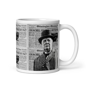 May include: A white ceramic mug featuring a black and white image of Winston Churchill and newspaper headlines. The headlines include "British Military Pact" and "Churchill Urges British". The mug has a curved handle.