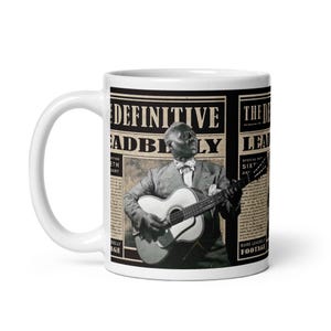 May include: White ceramic mug featuring a black and white image of a musician playing a guitar. The mug has text that reads "The Definitive Leadbelly" in a newspaper-style design. A great gift for music lovers.