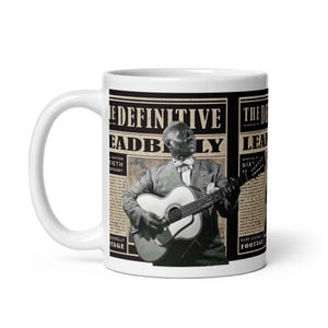 May include: White ceramic mug with a black and white image of a man playing a guitar. The image is surrounded by text that reads "The Definitive Leadbelly" and "Special 60th Anniversary Edition".