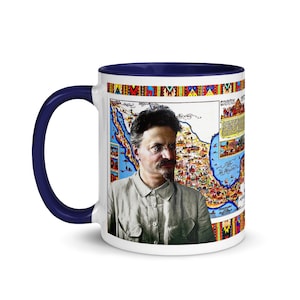 May include: White ceramic mug with a navy blue handle and interior. The mug features a portrait of a man with glasses and a mustache, along with a colorful map design. The rim of the mug has a decorative pattern.