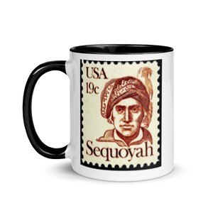 May include: White ceramic mug with a black rim and handle. The mug features a vintage US postage stamp with a portrait of Sequoyah, a Cherokee silversmith and inventor of the Cherokee syllabary. The stamp reads "USA 19c Sequoyah".