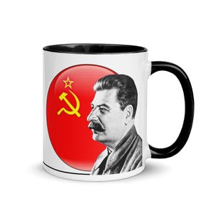 May include: White ceramic mug with a black interior and handle. The mug features a portrait of a man with a large moustache and a red circle with a yellow hammer and sickle and star.