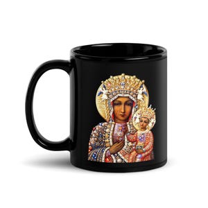 Könnte beinhalten: Schwarze Keramiktasse mit einem religiösen Bild einer Frau und eines Kindes, beide mit goldenen Kronen und Heiligenscheinen geschmückt. Das Bild ist detailreich und farbenfroh, vor schwarzem Hintergrund.
