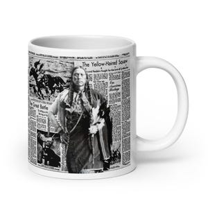 May include: White ceramic mug featuring a black and white image of a Native American man and newspaper clippings. The text on the mug includes "The Yellow-Haired Squaw" and "The Great Battle".