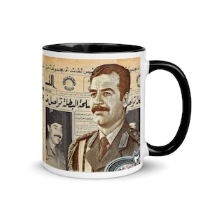 May include: A white ceramic mug with a black handle and interior rim, featuring a vintage-style graphic print of a man in a military uniform overlaid on a background of Arabic newspaper text and historical imagery with a sepia-toned aesthetic.