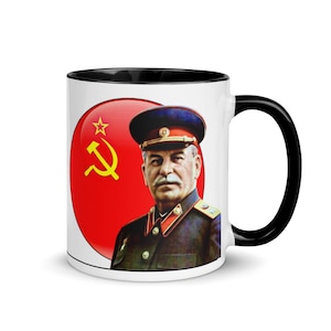 May include: White ceramic mug with a black handle and interior. The mug features a portrait of a man in a military uniform and a red circle with a yellow hammer and sickle. The mug is a novelty item.