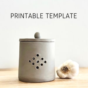 May include: A grey ceramic garlic keeper with a lid and holes for ventilation. A whole garlic bulb is sitting next to the keeper on a wooden surface. PRINTABLE TEMPLATE is written in black text at the top of the image.