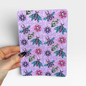 May include: A rectangular sticker sheet with a light purple background featuring a repeating pattern of blue moths, purple stag beetles, pink flowers with skull centers, purple flowers with skull centers, and small white floral sprigs.
