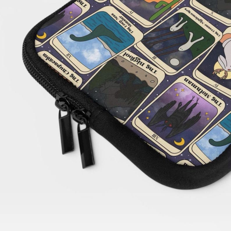 Puede incluir: Una funda negra con cremallera que presenta una cuadr&iacute;cula de cartas estilo tarot con ilustraciones de cr&iacute;ptidos. Las cartas visibles incluyen The Loch Ness Monster, The Bigfoot y The Mothman, con ilustraciones, n&uacute;meros romanos y texto.