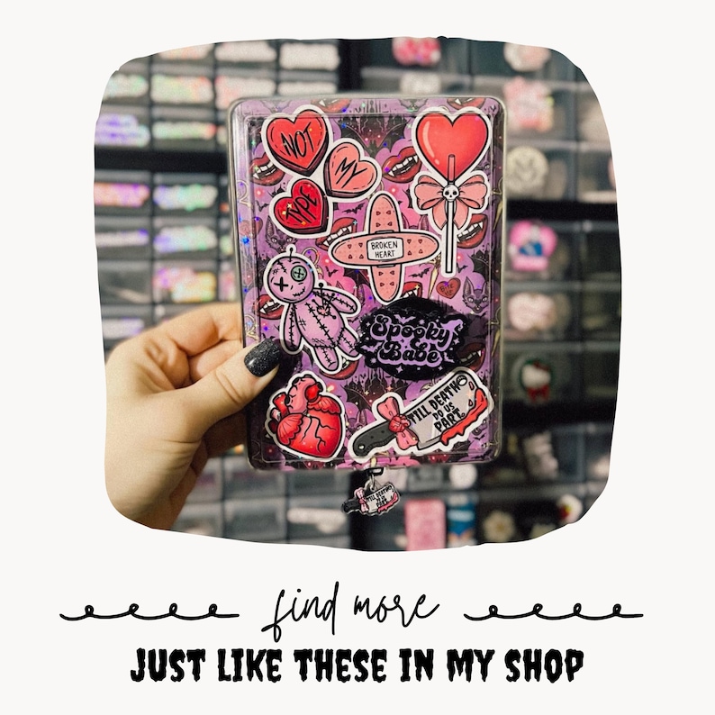 May include: A rectangular clear plastic card holder decorated with various stickers including a pink voodoo doll, a red anatomical heart, a lollipop, a bandage labeled broken heart, and a knife with the text Till Death Do Us Part.