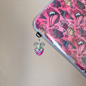 May include: A green praying mantis charm with a pink heart that says "Until Death" hanging from a silver chain. The charm is attached to a pink and white notebook with a pattern of lips, potion bottles, and hearts.