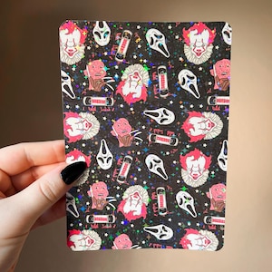 May include: A black rectangular sticker sheet with a repeating pattern of horror movie characters, including a clown, a ghost face, and Freddy Krueger. The design has a holographic, glittery effect.