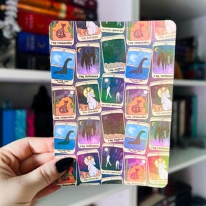 Puede incluir: Una tarjeta rectangular con ilustraciones de estilo tarot de criaturas críptidas como el Chupacabras, Mothman y Bigfoot. Cada carta tiene un diseño único con un fondo colorido, que incluye paisajes desérticos y cielos nocturnos. El texto en las cartas incluye los nombres de las criaturas.