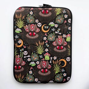 May include: Black laptop sleeve with a repeating pattern of moths, mushrooms, fireflies, and other woodland creatures. The background is black with white stars.