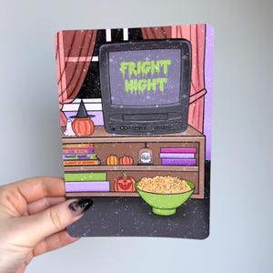 May include: A rectangular art print featuring a vintage television displaying the text FRIGHT NIGHT in green slime font. The scene includes a wooden shelf with books, small pumpkins, a skull in a glass dome, and a green bowl of popcorn.