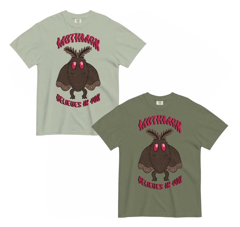 K&ouml;nnte beinhalten: Zwei kurz&auml;rmelige T-Shirts in hellem Salbeigr&uuml;n und Olivgr&uuml;n, jeweils mit einer zentralen Grafik einer braunen, mottenartigen Kreatur mit gro&szlig;en roten Augen, dar&uuml;ber der Text "MOTHMAN" und der Schriftzug "BELIEVES IN YOU" in roter Farbe.