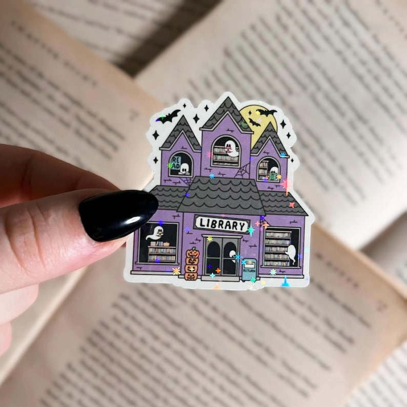 Pode incluir: Um adesivo roxo e branco de um pr&eacute;dio de biblioteca assombrado com a palavra "LIBRARY" acima da porta. O pr&eacute;dio tem janelas com fantasmas dentro lendo livros. H&aacute; ab&oacute;boras e estrelas ao redor do pr&eacute;dio.