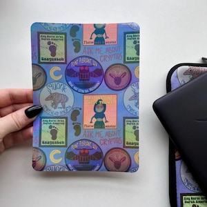 Peut inclure: Une feuille d'autocollants holographiques bleue et violette avec un motif répété de cryptides, notamment le Mothman, le Monstre de Flatwoods et le Sasquatch. Les autocollants comportent des textes tels que "Demandez-moi à propos des cryptides" et "Point Pleasant, WV".