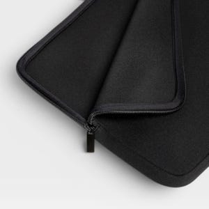 Puede incluir: Una funda para port&aacute;til negra hecha de un material suave y texturizado con esquinas redondeadas y una cremallera negra a juego. La funda est&aacute; parcialmente abierta, revelando el forro interior y el carril de la cremallera en el borde superior.