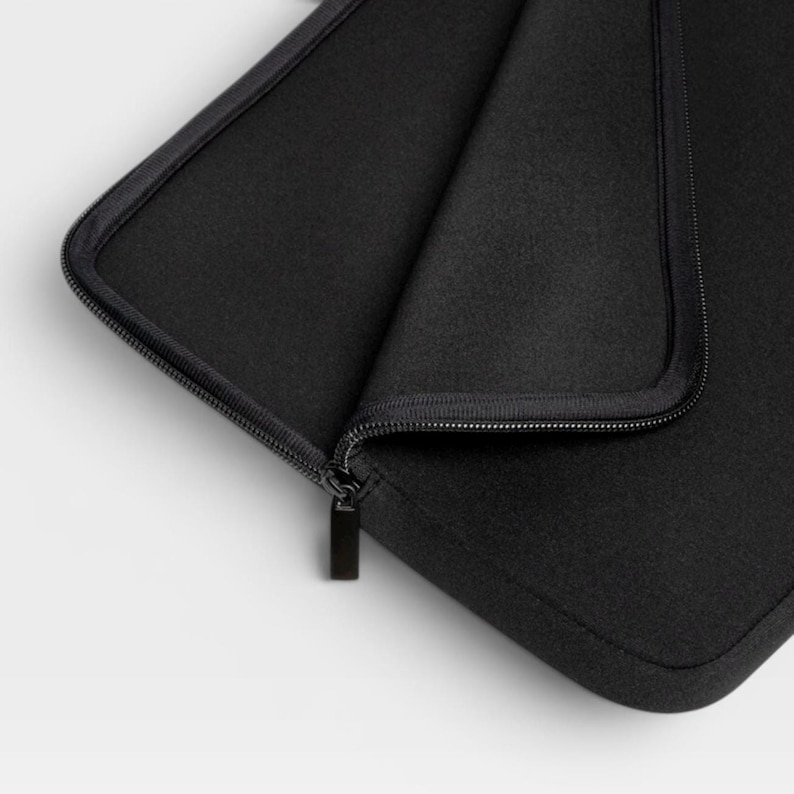Puede incluir: Una funda para port&aacute;til negra hecha de un material suave y texturizado con esquinas redondeadas y una cremallera negra a juego. La funda est&aacute; parcialmente abierta, revelando el forro interior y el carril de la cremallera en el borde superior.