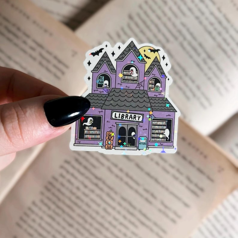 Pode incluir: Um adesivo roxo e branco de um pr&eacute;dio de biblioteca assombrado com fantasmas dentro. O adesivo tem detalhes de glitter e diz "LIBRARY" acima da porta da frente.