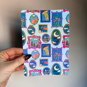 Peut inclure: Un autocollant rectangulaire avec un fond bleu clair présentant un motif répété d'illustrations encadrées. Les illustrations comprennent des paysages, des champignons, un croissant de lune avec des chauves-souris et une scène d'enlèvement extraterrestre.