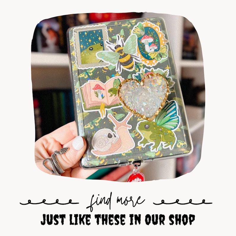 Puede incluir: Funda de tel&eacute;fono transparente decorada con pegatinas de una rana, una abeja, setas y un caracol. Un adorno en forma de coraz&oacute;n con purpurina iridiscente y ribete dorado est&aacute; centrado en la funda. El texto "find more JUST LIKE THESE IN OUR SHOP" est&aacute; en la parte inferior.