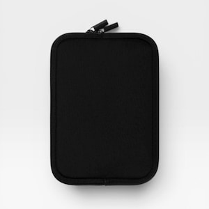 Puede incluir: Un estuche rectangular negro con cremallera y esquinas redondeadas. El exterior presenta una textura de tela negra s&oacute;lida con un cierre de cremallera negro a juego en la parte superior, que incluye dos peque&ntilde;os tiradores negros.