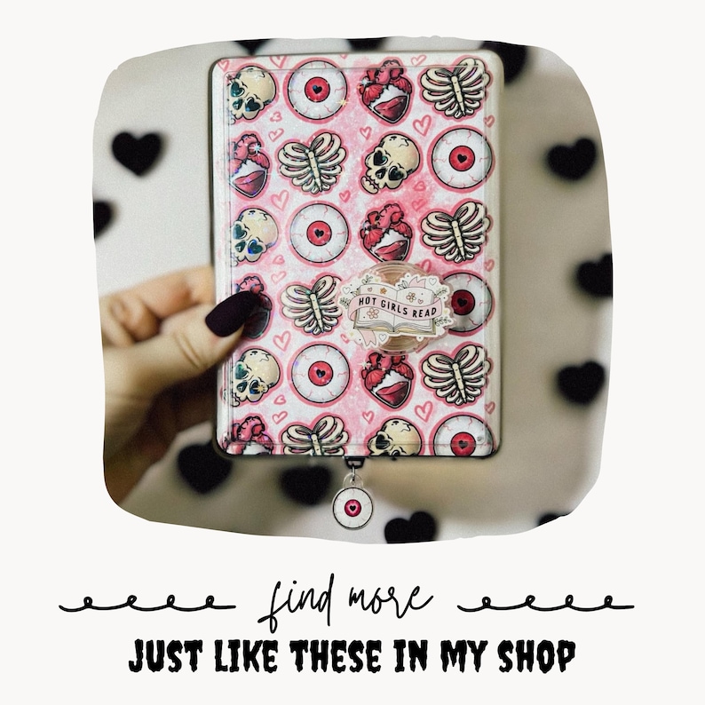 May include: A rectangular e-reader case with a pink background featuring a repeating pattern of skulls, eyeballs, rib cages, and hearts. A circular sticker on the front displays an open book with the text HOT GIRLS READ. A small circular charm hangs below.