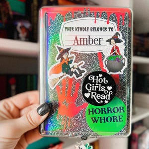 以下が含まれることがあります： 黒と銀のグリッターで覆われたKindleケース。魔女のステッカー、大釜のステッカー、「Hot Girls Read」と書かれたステッカー、「Horror Whore」と書かれたステッカーが付いています。ケースには、「This Kindle Belongs to Amber」と書かれたネームタグも付いています。