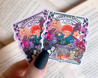 May include: Two stickers featuring the Sanderson Sisters from the movie Hocus Pocus. The stickers have a pink border and include the text "Sanderson Sisters 1693 Salem, Mass." The sisters are depicted in colorful outfits with a black cat and a bubbling cauldron.