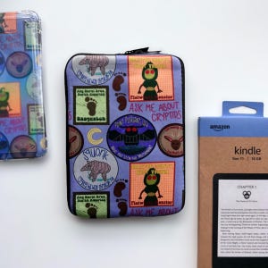 May include: A purple and blue Kindle cover with a pattern of cryptids, including the Mothman, Sasquatch, and the Flatwoods Monster. The text on the cover reads "Ask me about cryptids".