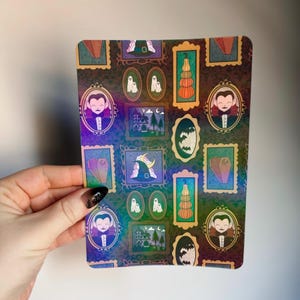 Peut inclure: Un autocollant rectangulaire sur le thème d'Halloween avec un motif répété d'illustrations encadrées. Les illustrations comprennent un vampire, des citrouilles, des fantômes, une maison hantée, un cercueil et un chapeau de sorcière. Le fond est de couleur sombre et irisée.