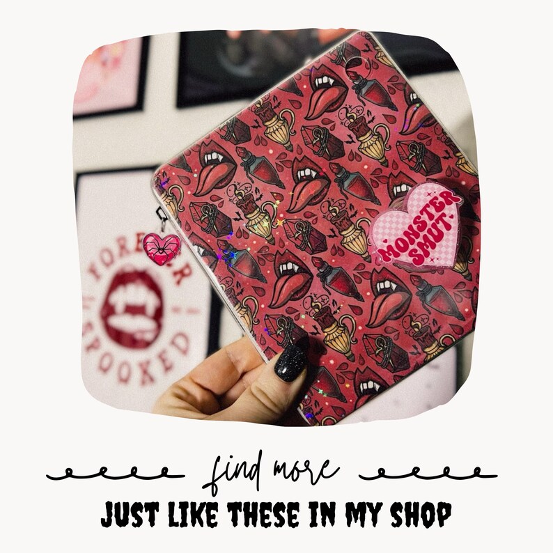 May include: A square zippered pouch with a red background featuring a repeating pattern of vampire mouths, fangs, and potion bottles. A pink heart-shaped sticker with the text MONSTER SMUT is attached to the front, and a small heart charm hangs from the zipper.