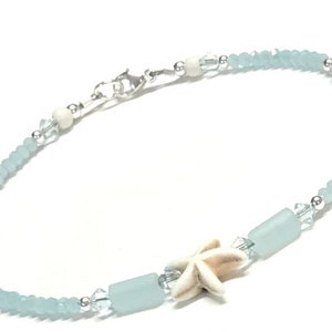 May include: Ankle bracelet featuring light blue faceted beads, clear crystal accents, and a white starfish charm. The bracelet includes cylindrical light blue beads and a silver-tone clasp. A delicate piece of jewelry.
