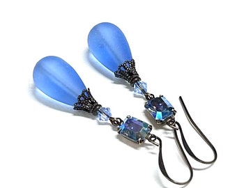 May include: A pair of dangle earrings with light blue teardrop-shaped glass beads, antique bronze filigree accents, and iridescent blue crystal accents.