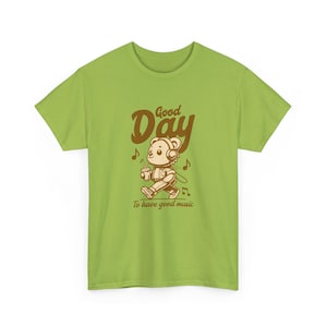 Pode incluir: Camiseta verde limão com um urso de desenho animado usando fones de ouvido e segurando uma xícara de café. O texto "Good Day" e "To have good music" está impresso acima e abaixo da ilustração do urso.