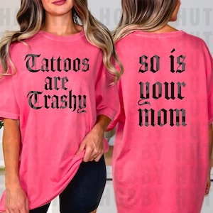 May include: A bright pink t-shirt with the text "Tattoos are Trashy" on the front and "So is your Mom" on the back, in a gothic font. The shirt has short sleeves and a relaxed fit.