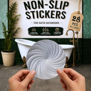 Op de afbeelding: Een ronde, zilverkleurige antislipsticker met een getextureerd wervelpatroon. De tekst op de verpakking luidt: LELUCA CREATIONS, NON-SLIP STICKERS FOR SAFER BATHROOMS, 28 PCS IN A PACK, A MUST-HAVE FOR EVERY HOME, PERFECT FOR ELDERLY & FAMILIES, A THOUGHTFUL & USEFUL GIFT.