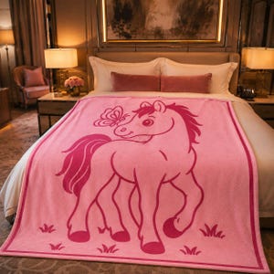 May include: A pink blanket with a cartoon horse and butterfly design. The horse is outlined in a darker shade of pink. The blanket is placed on a bed with white sheets. The blanket has a border.