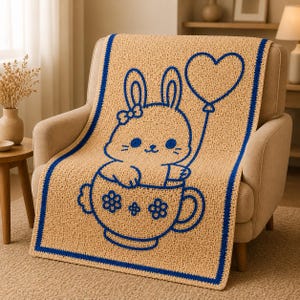 May include: A beige crochet blanket with a blue border and a blue cartoon bunny design. The bunny is in a teacup and holding a heart-shaped balloon. The blanket is draped over a beige armchair.
