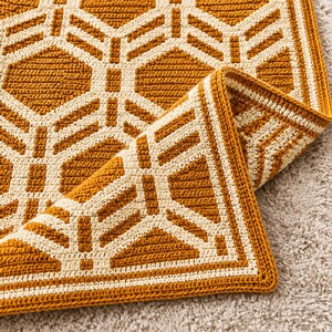 May include: A rectangular crochet blanket featuring a geometric pattern of mustard yellow and cream white interlocking hexagons. The fabric has a dense, textured stitch construction with a folded corner revealing the reverse side.
