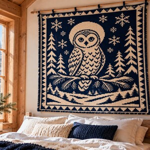 May include: A square wall hanging featuring a dark blue and cream knit pattern of an owl perched on a pine branch. The design includes surrounding pine trees and snowflakes, finished with a decorative border and hung from a wooden rod.