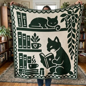 May include: A cream-colored crochet blanket featuring a dark green design of two cats, bookshelves, potted plants, and a steaming mug. The border consists of a repeating scalloped pattern in dark green and cream, framing the entire rectangular piece.