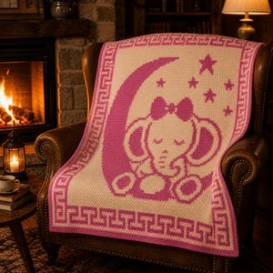 May include: A pink and cream-colored baby blanket with an elephant design. The blanket features a pink elephant sitting on a crescent moon, surrounded by stars. The border has a Greek key pattern.