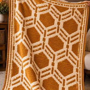 May include: A rectangular crochet blanket featuring a repeating geometric pattern of mustard yellow and cream white hexagons. The design includes a thick, textured border with a repeating square motif framing the central honeycomb structure.