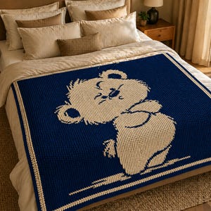 May include: A navy blue and cream knitted blanket with a cartoon bear design. The bear is in a playful pose, with a cream border and a textured appearance. The blanket is displayed on a bed with neutral-toned bedding.