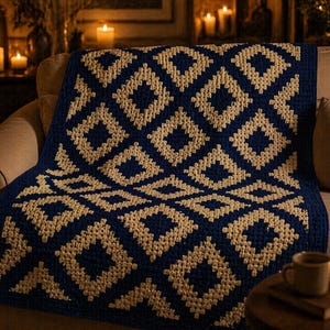 May include: A navy blue and beige crocheted blanket with a geometric diamond pattern. The blanket is draped over a beige sofa. The blanket's design adds warmth and texture. The scene is lit by candlelight, creating a cosy atmosphere.