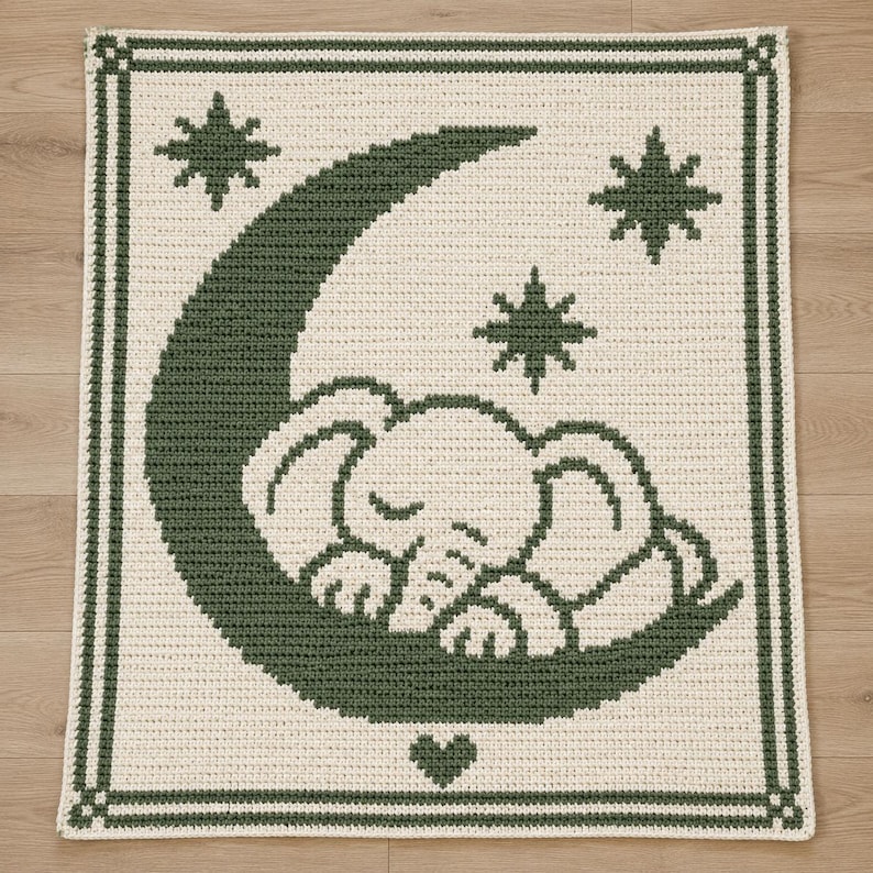 May include: A rectangular crochet blanket featuring a cream-colored background with a dark green border. The center displays a large dark green crescent moon with a sleeping elephant resting on it, surrounded by three dark green stars and a small heart.